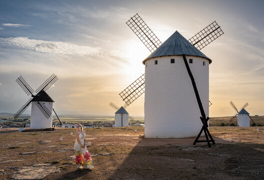Traditional windmill illuminated by warm sunset light with a female traveler in the foreground in Campo de Criptana, one of the most recognizable locations in the region of La Mancha.