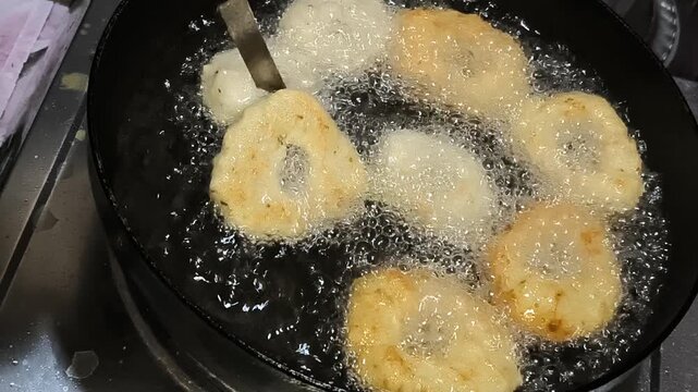 Turning over golden crispy tootu vada in hot frying oil with spatula