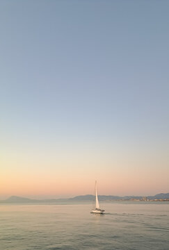 Minimalist seascape with a white sailboat cruising on calm sea water at sunset, pastel gradient sky background with copy space.