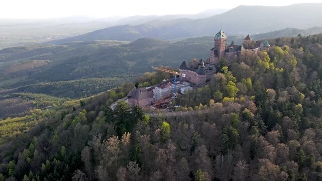 Aerial view of medieval castle undergoing restoration with scaffolding on tower and conservation work visible on sandstone walls. Heritage preservation project with crane and masonry repair in Vosges
