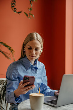 Woman working remotely using smartphone and laptop in cafe