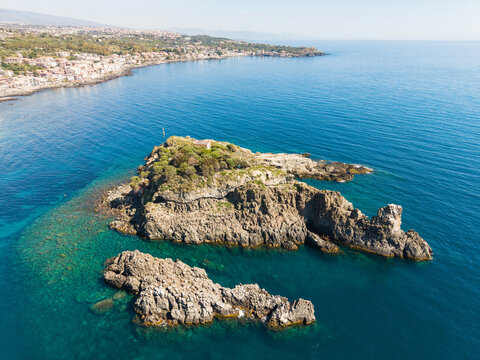 Aerial view of the Islands of the Cyclops featuring volcanic rock formations surrounded by turquoise Mediterranean waters near the coast of Aci Castello, Italy.