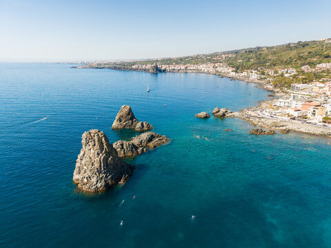 Aerial view of the Islands of the Cyclops volcanic sea stacks rising from the turquoise Mediterranean sea along the coast of Aci Castello, Italy.
