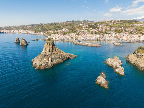 Aerial view of the Islands of the Cyclops basalt rock formations rising from the blue Mediterranean sea near the coastal town of Aci Castello, Catania, Italy.