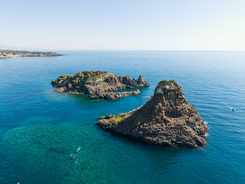 Aerial view of Islands of the Cyclops featuring volcanic rock formations and turquoise Mediterranean waters along the coast of Aci Castello, Catania, Italy.