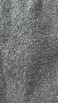 Close-up rolled roofing granules texture, coarse mineral surface on bitumen membrane, grey aggregate fragments, protective coating
