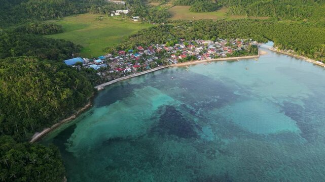 Scenic aerial dolly along the Virac coastline in Catanduanes, Philippines with shallow reefs, clear coastal waters, a seaside village, and lush greenery