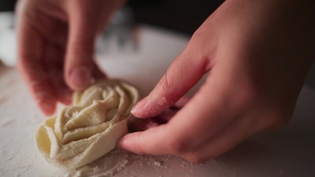Close-up of hands shaping dough on floured surface. Fingers gently press and fold dough layers. Process highlights homemade pastry preparation. Suitable for cooking, bakery, or food tutorials