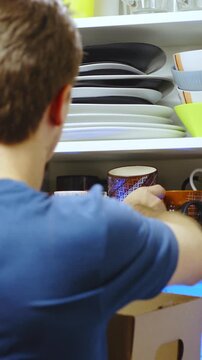 Person packs cups from kitchen closet into cardboard box