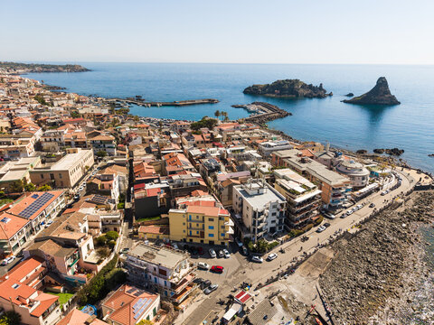 Aerial view of the Islands of the Cyclops and the coastal town with terracotta rooftops and a small harbour in Aci Castello, Italy.