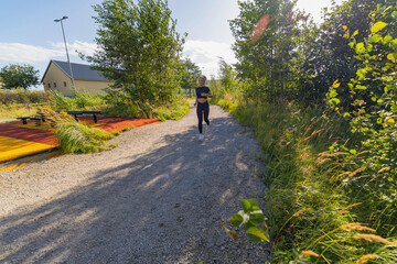 Fototapeta premium Woman jogging on a scenic trail surrounded by greenery and sunlight