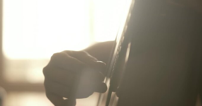 Cinematic close-up of hands playing a classical acoustic guitar in warm golden sunlight. Soft natural light highlights the wooden texture, vibrating strings, and elegant finger
