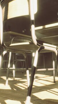 Sunlight shines through the window onto the wooden floor in the classroom. Empty chairs and tables are arranged in the space. The scene shows a typical school environment.