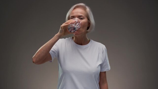 Old woman drinking water, smile mature woman for health, vision or wellness. Beverage, happy pensioner person. Senior female hold glass with aqua for hydration, liquid, fluid and minerals for thirsty