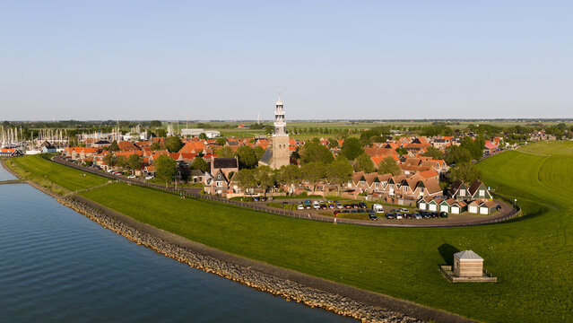 Aerial view of Grote Kerk church tower and traditional red-roofed houses along the green dike by the sea in Hindeloopen, Friesland, Netherlands.