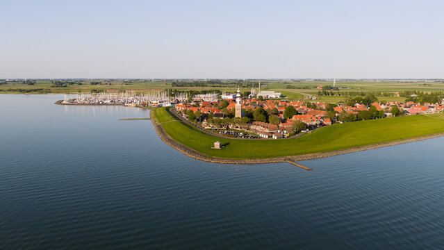 Aerial view of the Grote Kerk church and historic red rooftops surrounded by a green dike and a harbor filled with sailboats in Hindeloopen, Friesland, Netherlands.