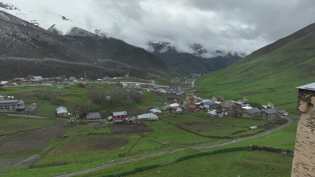 Aerial view of Lamaria church complex with traditional Svan tower in Ushguli, Svaneti region, Georgia, medieval stone fortress and cemetery in Caucasus mountains under cloudy sky.