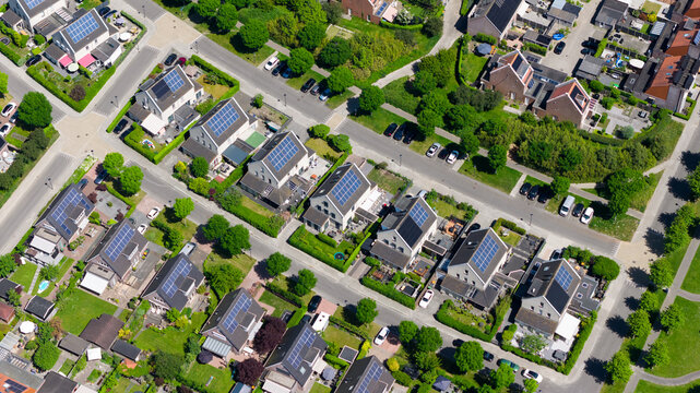Aerial view of modern residential houses with solar panels on rooftops, lush green gardens, and quiet suburban streets in Heerhugowaard, North Holland, Netherlands.