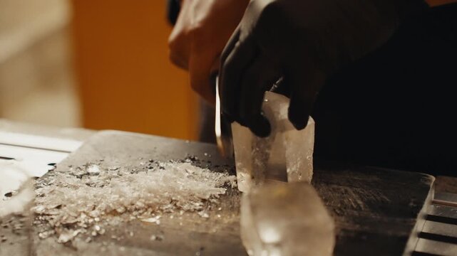 Bartender carving clear ice cube with knife