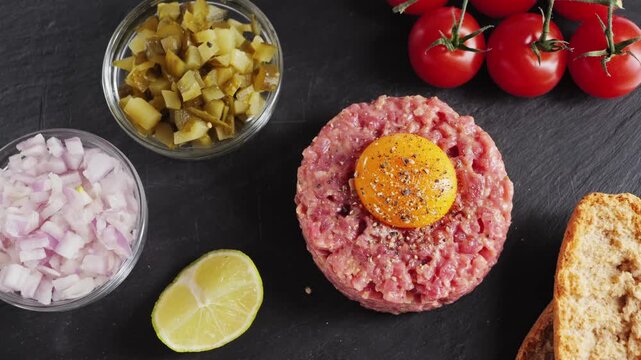 Raw beef tartare with sauce on a black stone tray. Homemade tartare with onion, capers, and egg yolk. High-quality 4K video. High quality 4k footage