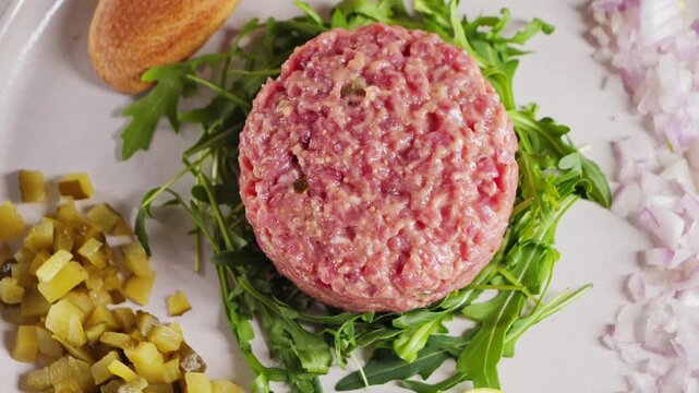 Beef tartare with arugula and capers, onions, bread slices and lime wedges on a ceramic plate. High quality 4k footage