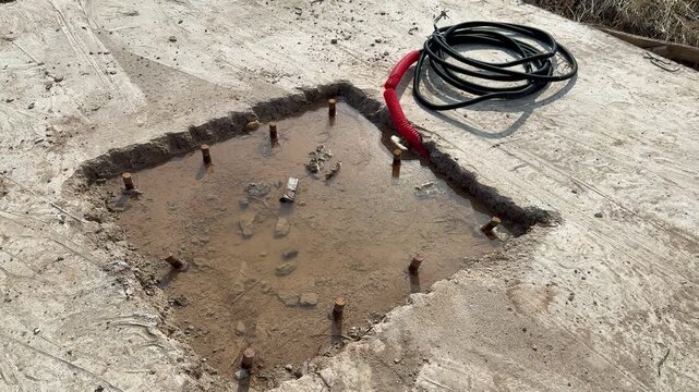Ground hole with bolts and cable installer preparing concrete foundation for vertical billboard pole, coiled power cable