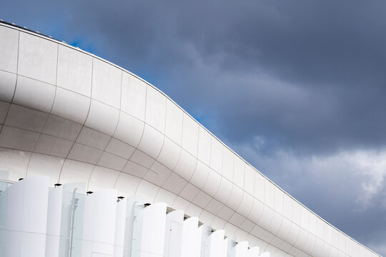 Curved architecture sweeps above columns as a white facade meets stormy sky, giving the urban building edge strong scale and depth.