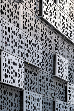 Perforated facade architecture creates a dotted geometric pattern across an urban building, where sharp panels add texture and perspective.