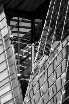 Monochrome architecture rises through a narrow urban passage, where glass facade reflections and geometric building lines frame vertical light.