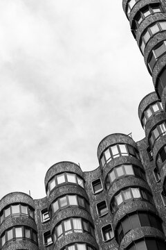 Monochrome architecture curves upward as a cylindrical building facade repeats windows, creating urban geometric rhythm against a pale sky.