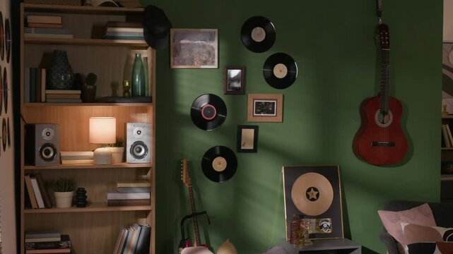 Interior shot of musicians apartment with gold award plaque displayed on shelf, speakers in bookcase, guitar hanging on wall decorated with vinyl records