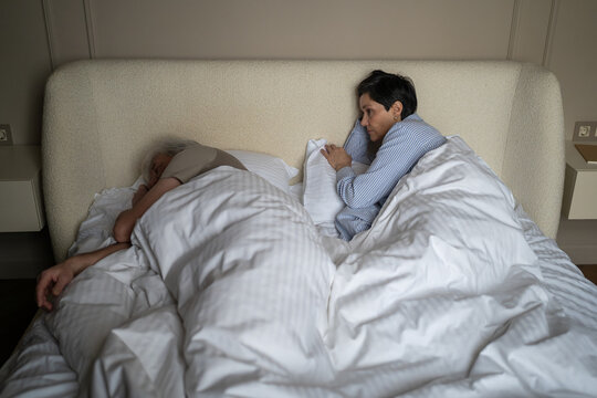 Married elderly couple struggles and health issues, senior woman with insomnia suffering from husband loud snoring at night, sleepless female lying in bed while man enjoying night sleep and snoring
