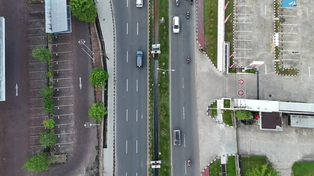 A view from above of an urban highway featuring a parking area, passing cars, a median, and sidewalks in West Borneo, Indonesia.