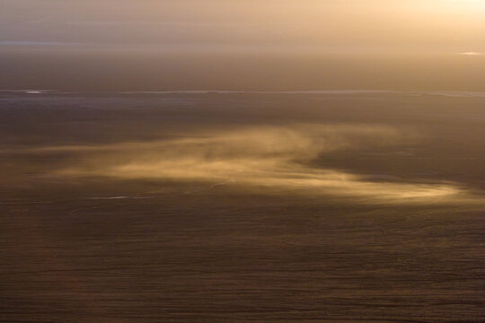 Aerial view of the vast desert landscape with dust blowing across the arid ground during golden hour near Laguna Baltinache in San Pedro de Atacama, Antofagasta, Chile.
