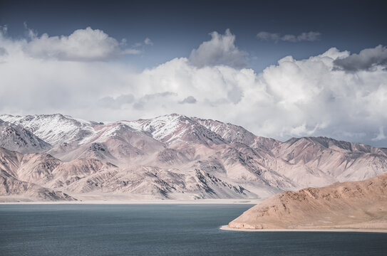 Landscape in the Pamir Mountains with a blue lake Yashilkul in the Tien Shan, a panoramic view of the highlands with snow-capped rocky peaks and the blue waters of the lake