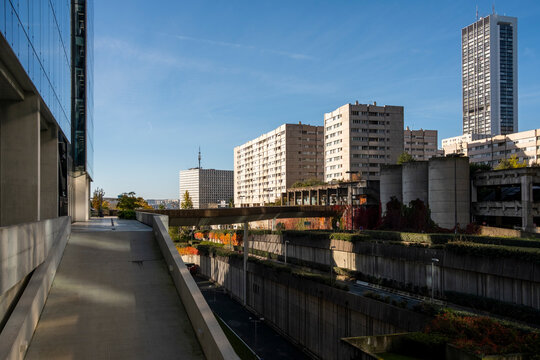 Walkway beside a canal in La Defense leads toward urban buildings, where skyline architecture opens across a Paris France promenade with autumn planting.
