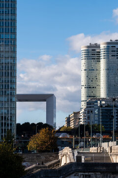 Grande Arche stands within La Defense skyline as highrise tower architecture and urban Paris France forms align beneath bright clouds and autumn trees.