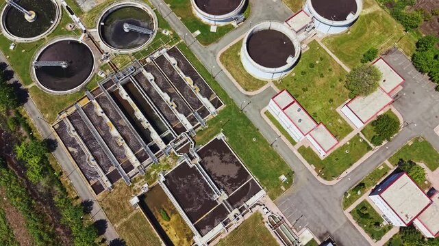 Aerial view aging sewage treatment facility showing decaying basins and algae growth, drone imaging for risk assessment and inspector planning, dark pools