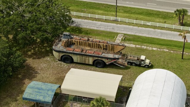 Aerial view of a large amphibious military landing craft and a transport truck parked on a grassy field near metal hangars Green Cove Springs, Florida, United States.