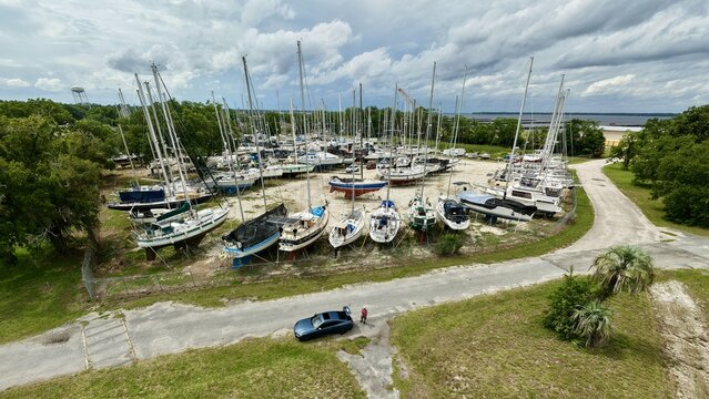 Aerial view of numerous sailboats resting on dry storage stands in a boatyard with a man in a red shirt standing by a parked car in Green Cove Springs, Florida, United States.