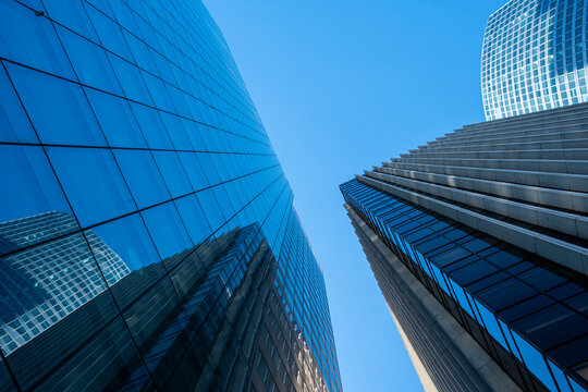 Glass skyscraper architecture rises between mirrored facades, where blue sky opens above sharp urban lines and vertical towers in a clean frame.