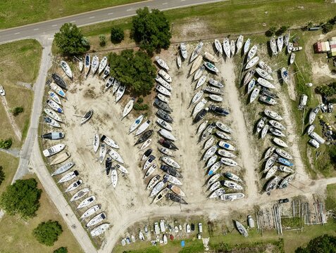 Aerial view of numerous sailboats parked in neat rows at a dry storage boatyard surrounded by green trees and a paved road in Green Cove Springs, Florida, United States.