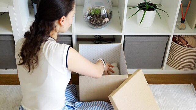 Young woman putting an old toy away in organizing storage box in calm home interior. Sustainable living and mindful home routine concept