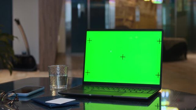 Close up of laptop displaying green screen with tracking markers on table alongside passport with key card and smartphone, perfect for inserting custom travel booking website or application