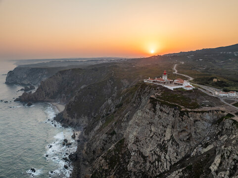 Aerial view of Cape Roca Lighthouse perched on rugged cliffs overlooking the Atlantic Ocean during a golden sunset Colares, Lisboa, Portugal.