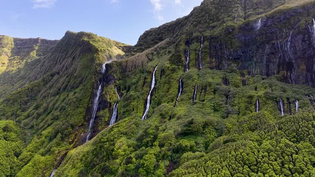 Scenic panoramic landscape of cascading waterfalls flowing through lush volcanic cliffs at Poco da Ribeira do Ferreiro in the Azores Portugal