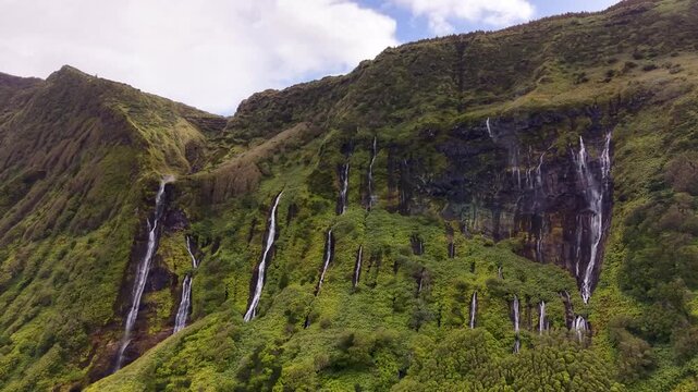 Cinematic landscape of cascading waterfalls flowing down lush volcanic cliffs at Poco da Ribeira do Ferreiro in the Azores Portugal