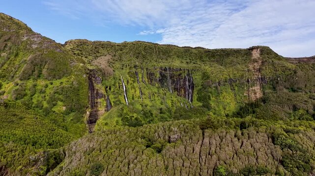Scenic wide landscape of cascading waterfalls flowing through lush volcanic cliffs at Poco da Ribeira do Ferreiro in the Azores Portugal