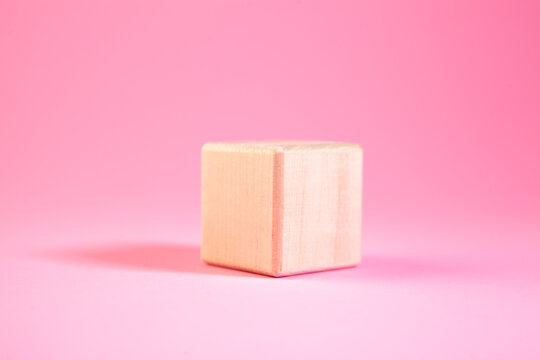 Wooden cube on a pink background. Minimalism style.