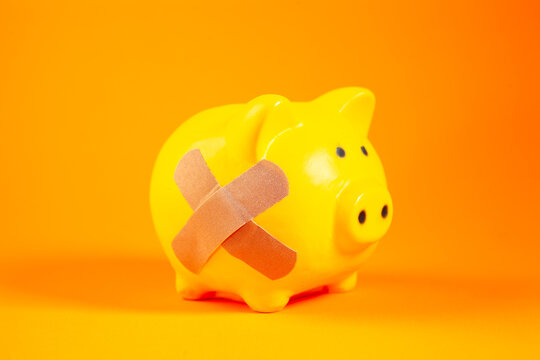 Piggy bank with bandage on orange background. Concept of financial aid
